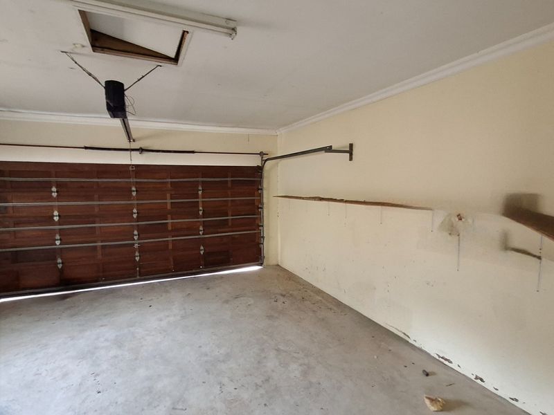 A functional garage space featuring a wooden sectional door, concrete flooring, and built-in wall shelving, showing signs of wear and maintenance requirements.