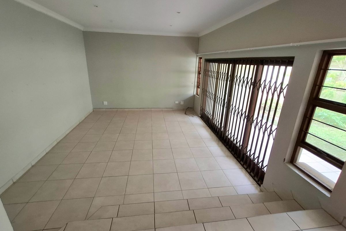 An empty, tiled living room featuring recessed lighting and a large sliding door with a security gate leading to the exterior.
