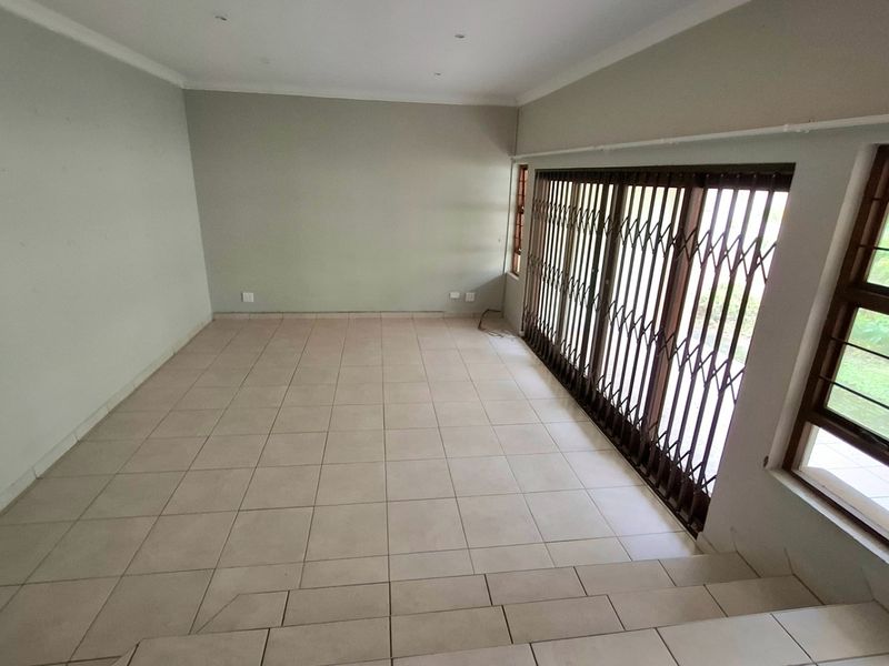 An empty, tiled living room featuring recessed lighting and a large sliding door with a security gate leading to the exterior.