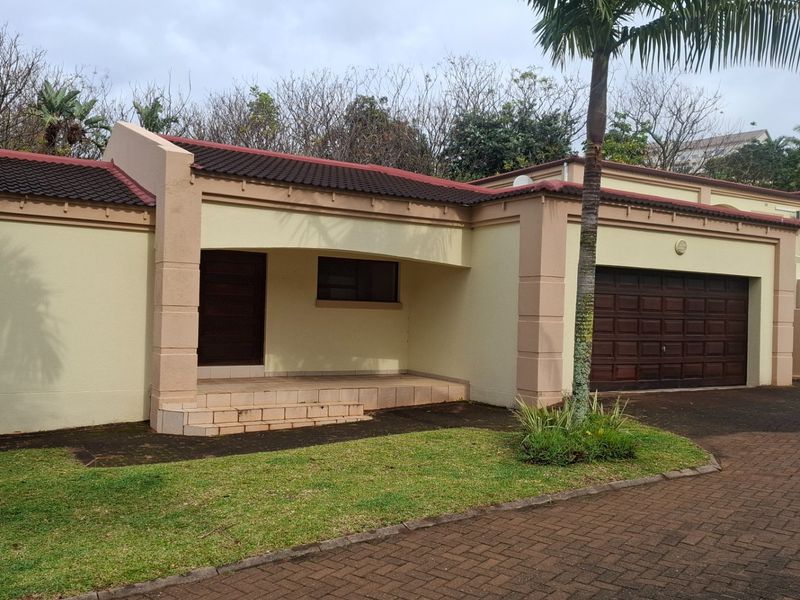 Front elevation of a townhouse featuring a paved driveway, double garage, and a covered entrance porch with brick steps.