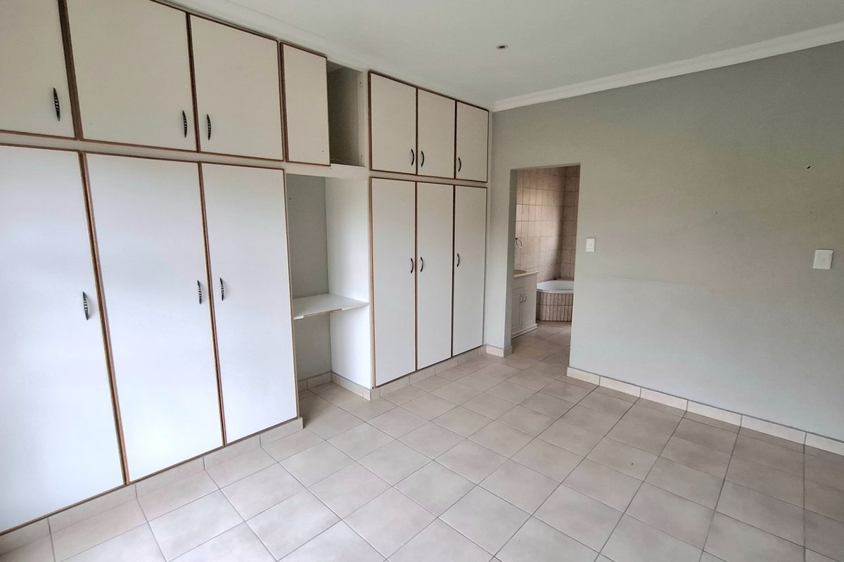 A spacious bedroom featuring extensive built-in cabinetry, neutral tiled flooring, and direct access to an en-suite bathroom.