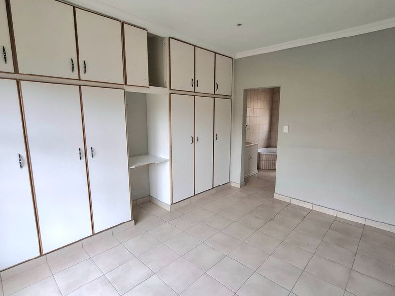 A spacious bedroom featuring extensive built-in cabinetry, neutral tiled flooring, and direct access to an en-suite bathroom.