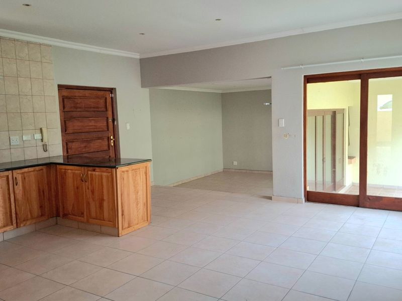 Spacious open-plan living and kitchen area featuring wooden cabinetry, granite countertops, tiled flooring, and large sliding doors leading to the exterior.