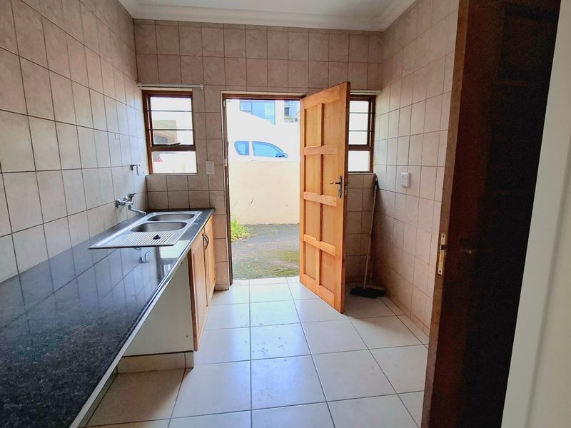 A functional scullery area featuring tiled walls, a double sink with granite countertops, and direct access to the exterior.