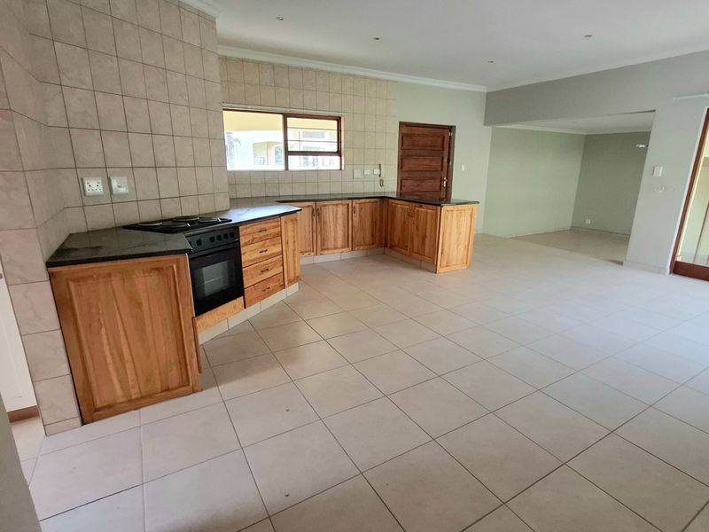 Spacious open-plan kitchen and living area featuring wooden cabinetry, granite countertops, built-in appliances, and neutral tiled flooring throughout.