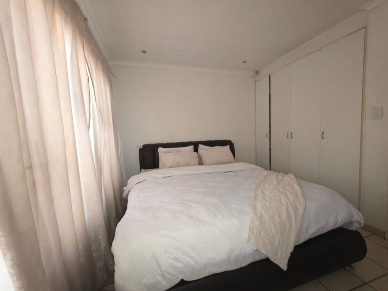 A functional bedroom featuring built-in cupboards, tiled flooring, and recessed downlighting, providing a neutral foundation for personal styling.