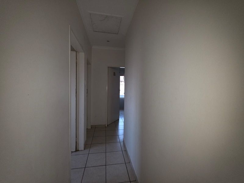 A simple, empty hallway featuring neutral tiled flooring and a ceiling access hatch, providing access to various rooms within the townhouse.