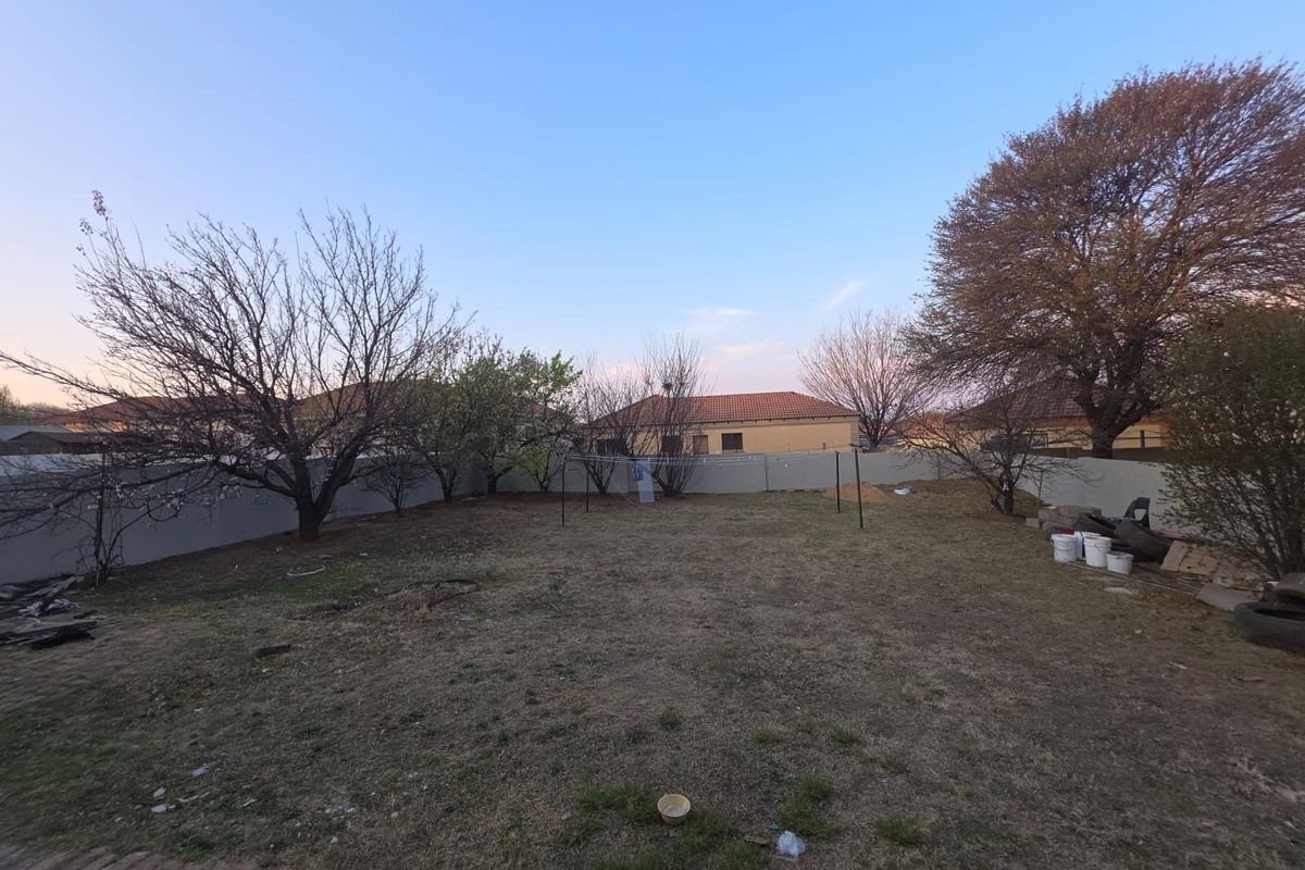 A spacious rear garden area featuring a perimeter wall and established trees, offering potential for landscaping and outdoor development.