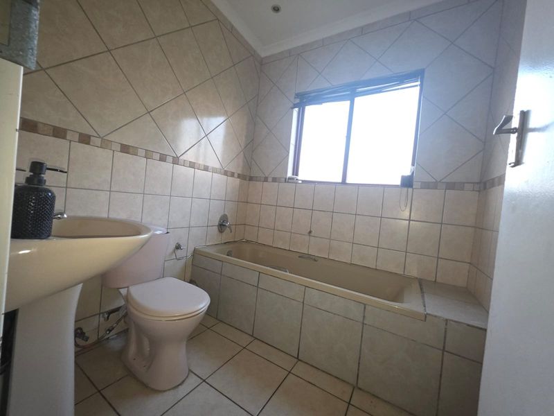 A functional bathroom featuring a pedestal basin, toilet, and a built-in bathtub with neutral wall and floor tiling.