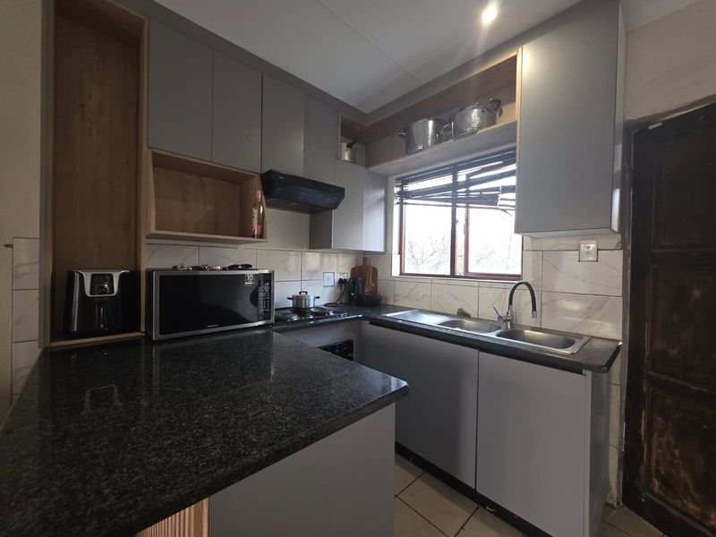 A functional kitchen featuring modern grey cabinetry, granite countertops, a double basin sink, and a tiled backsplash with a window for natural light.