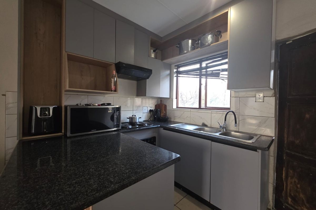 A functional kitchen featuring modern grey cabinetry, granite countertops, a double basin sink, and a tiled backsplash with a window for natural light.