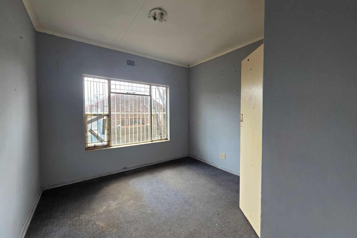 An empty bedroom featuring built-in cupboards, carpeted flooring, and security bars on the window. The room requires cosmetic updates and repairs.