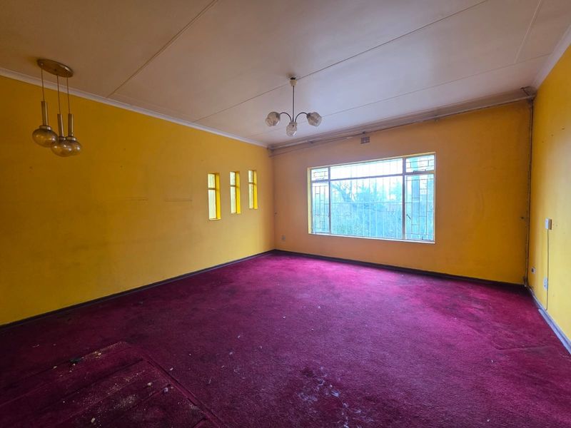 Spacious living room featuring large windows with security bars, dated yellow walls, and worn carpeting, offering a blank canvas for renovation.