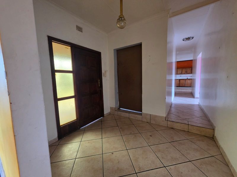 An entry foyer featuring tiled flooring, a timber front door with a glass sidelight, and a direct view into the hallway and kitchen area.