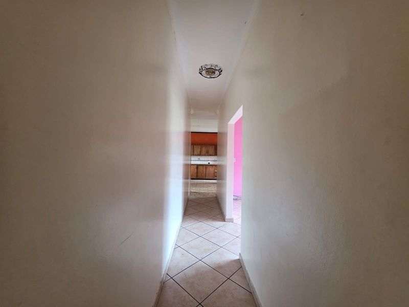 A narrow interior hallway featuring tiled flooring and a central ceiling light fixture, providing access to adjacent living areas.