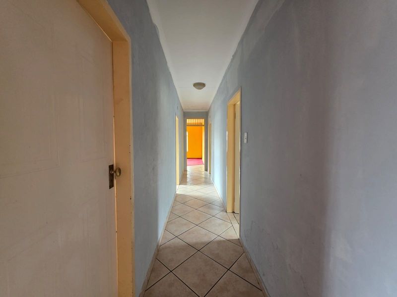 A long, empty hallway featuring tiled flooring and multiple internal door access points, requiring cosmetic updates to the wall finishes.