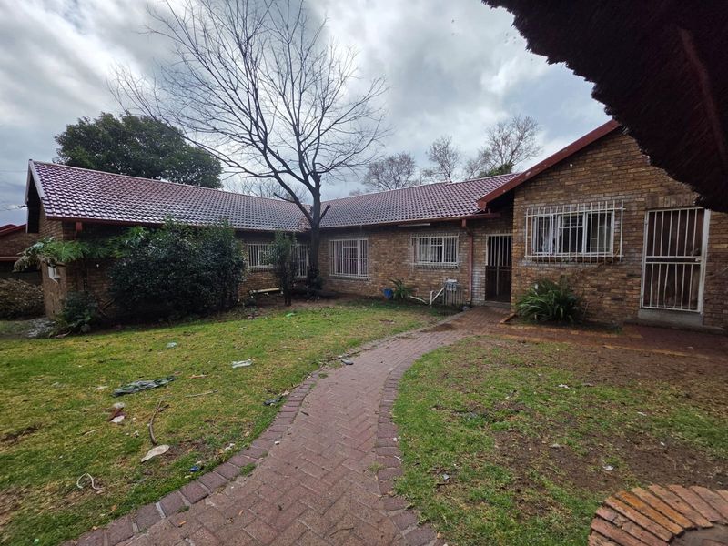 Rear view of a face brick townhouse featuring a tiled roof, security bars on windows, and a paved walkway leading through the garden area.