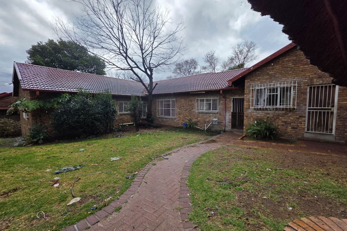 Rear view of a face brick townhouse featuring a tiled roof, security bars on windows, and a paved walkway leading through the garden area.