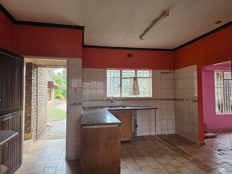 An empty, dated kitchen featuring tiled splashbacks, laminate countertops, and direct access to an outdoor patio area.