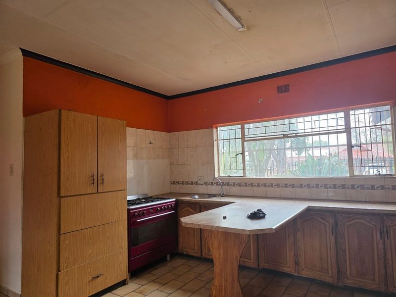 A dated kitchen featuring wooden cabinetry, a gas stove, tiled backsplash, and a breakfast counter, offering significant potential for modernization and renovation.