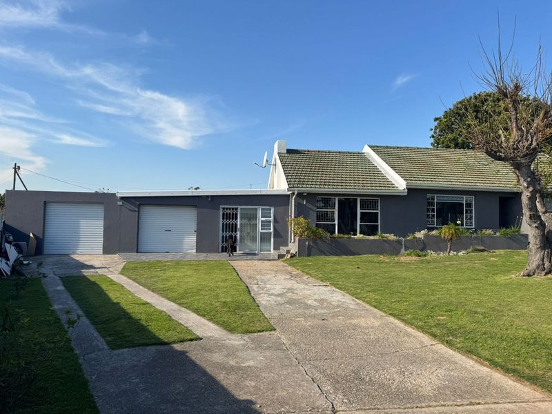 Front exterior view of a single-story house featuring a double garage, concrete driveway, and a well-maintained lawn under a clear blue sky.