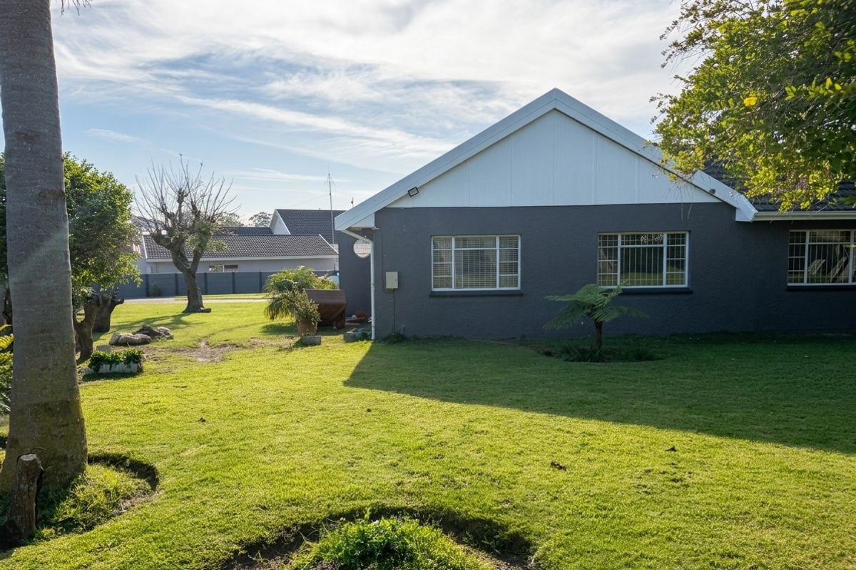 A view of the rear exterior of the house featuring a gabled roof, dark grey rendered walls, and a spacious lawn area.