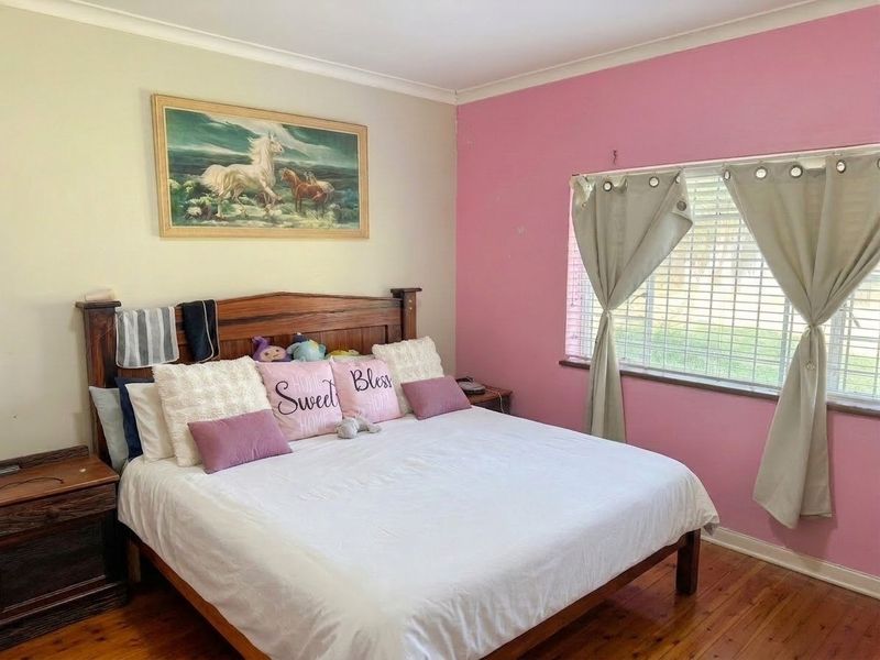 A bedroom featuring timber flooring, cove cornicing, and a window fitted with venetian blinds, offering a functional space with potential for cosmetic updates.