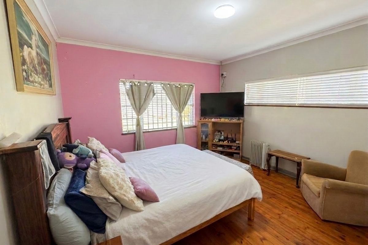A spacious bedroom featuring original hardwood flooring, security bars on the windows, and a neutral ceiling with cove cornicing.