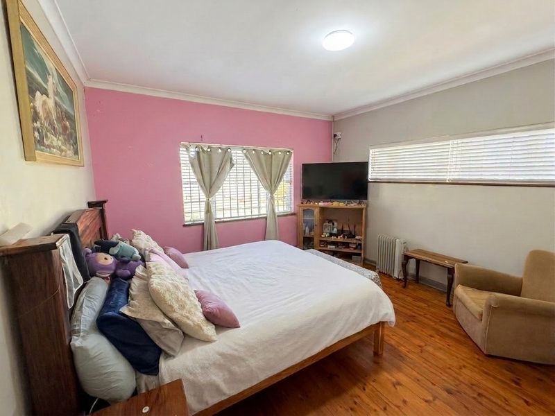 A spacious bedroom featuring original hardwood flooring, security bars on the windows, and a neutral ceiling with cove cornicing.