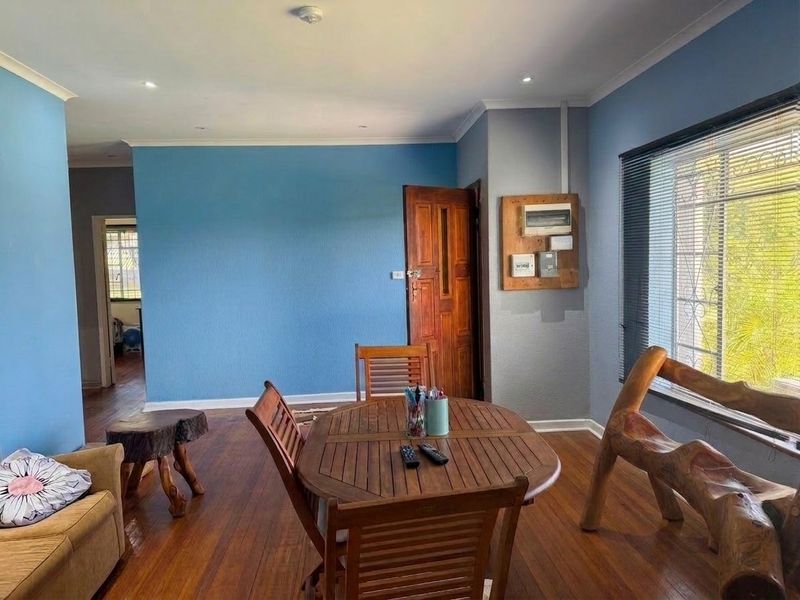 A living area featuring hardwood flooring, blue painted walls, and a visible electrical distribution board, offering a functional space with potential for modernization.