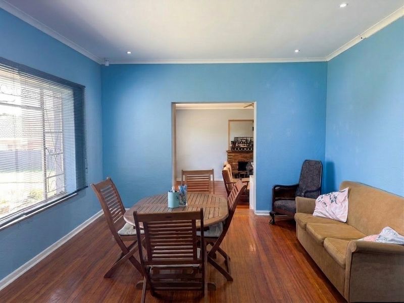 A living room featuring hardwood flooring, recessed lighting, and large windows with venetian blinds, leading into an adjacent room with a fireplace.