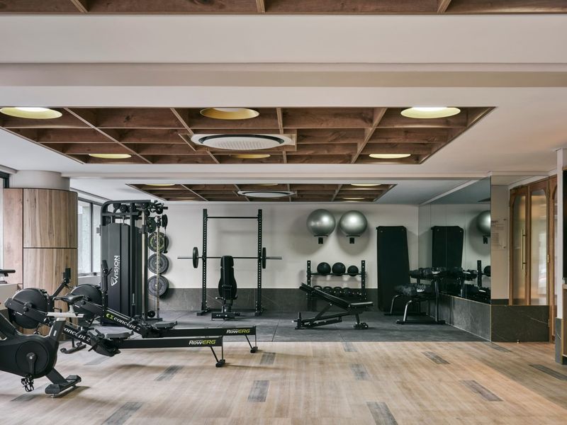 A modern, well-equipped gym featuring a coffered timber ceiling, mirrored walls, and a combination of laminate and rubber flooring.