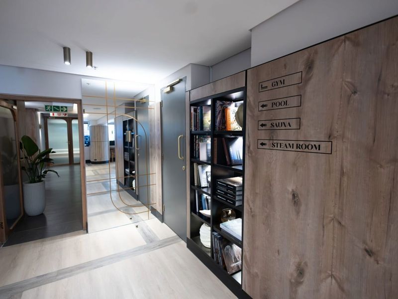 A modern, well-lit hallway featuring wood-grain paneling, integrated shelving, and clear directional signage leading to building amenities.
