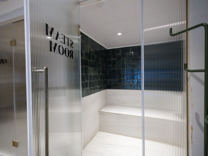 A modern steam room featuring a fluted glass door, built-in bench seating, and stylish dark tiled wall accents.