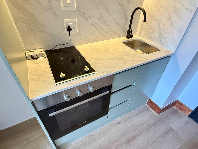 Compact modern kitchen featuring a built-in Bosch oven, electric hob, marble-look surfaces, and a sleek matte black faucet.