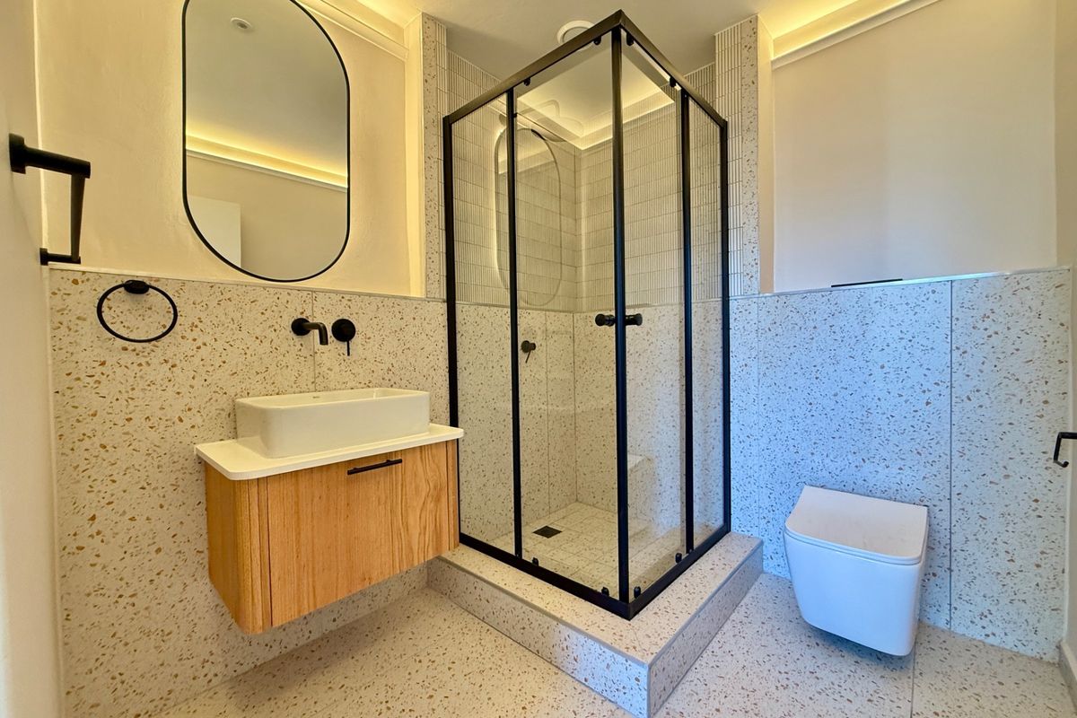Modern bathroom featuring terrazzo tiling, a wall-mounted vanity with vessel sink, a walk-in shower with black frame, and a wall-hung toilet.