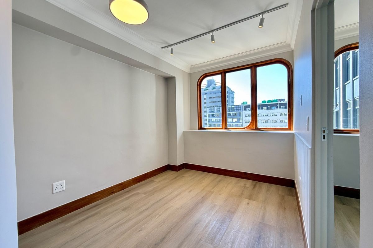 A bright, empty bedroom featuring modern laminate flooring, timber-framed windows, and contemporary track lighting, offering a clean and neutral space ready for furnishing.