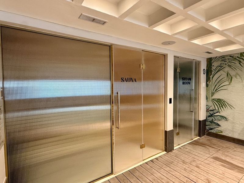 A well-maintained wellness area featuring a dedicated sauna and steam room with modern glass doors, coffered ceilings, and decorative mosaic wall tiling.