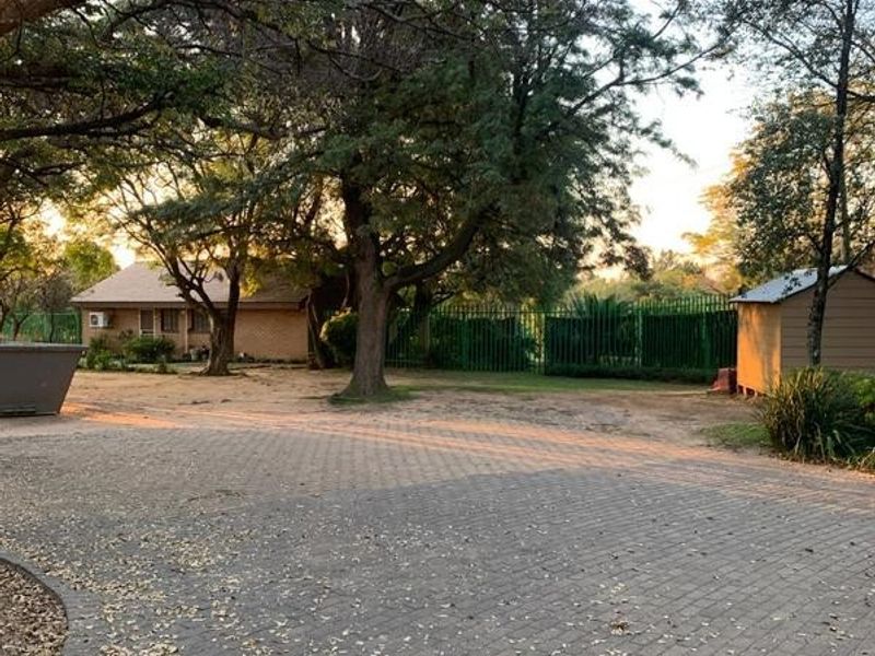 A spacious paved driveway leading to the main residence, featuring mature trees, perimeter fencing, and an additional outbuilding on the property.