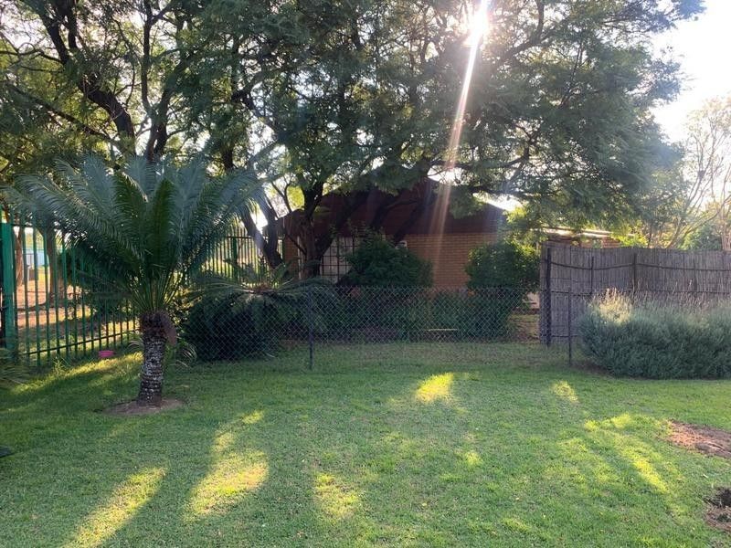 A private garden area featuring established trees, a well-maintained lawn, and secure perimeter fencing with natural reed screening.