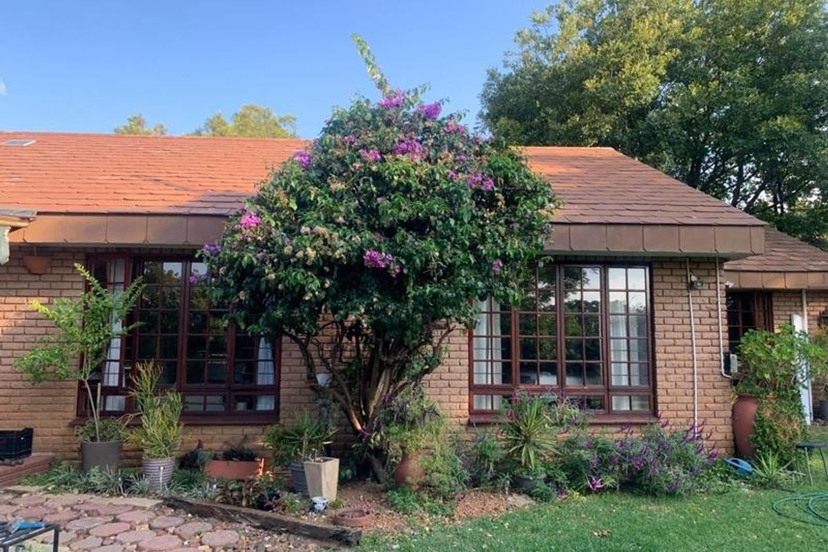 Rear view of a brick-faced small holding dwelling featuring timber-framed windows, a tiled roof, and established garden landscaping.
