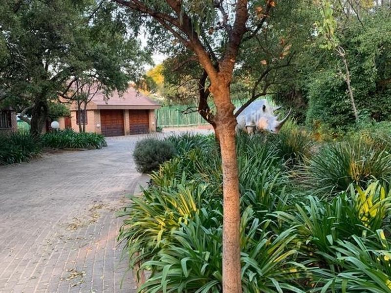 A view of the property entrance featuring a paved driveway, established garden with a brick retaining wall, and a double garage.