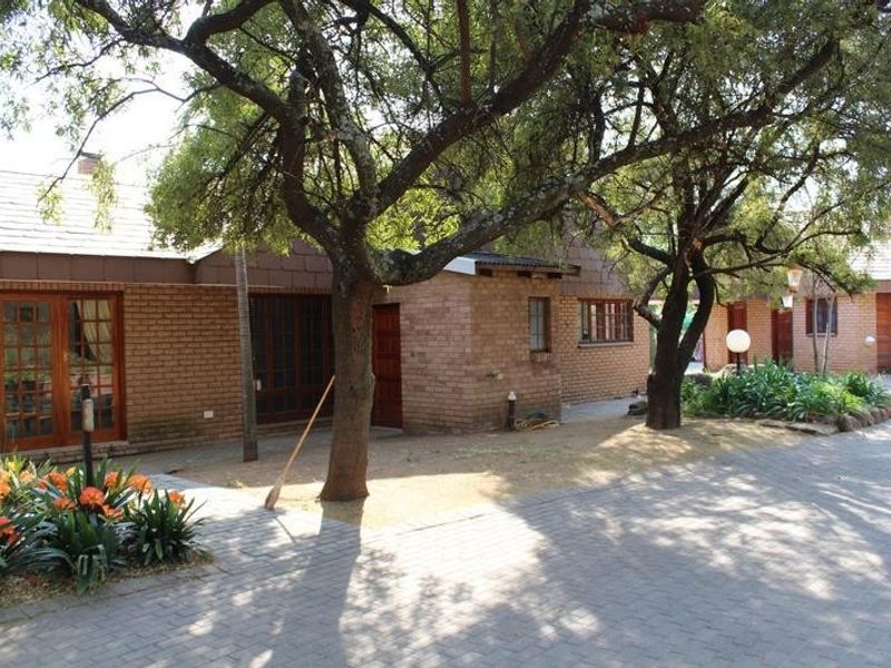 Front view of a brick-faced small holding property featuring a paved driveway, mature trees, and timber-framed doors and windows.