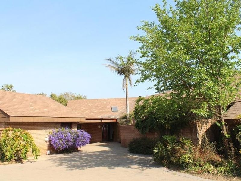 Front elevation of a brick-built small holding featuring a tiled roof, paved driveway, and established garden surroundings.