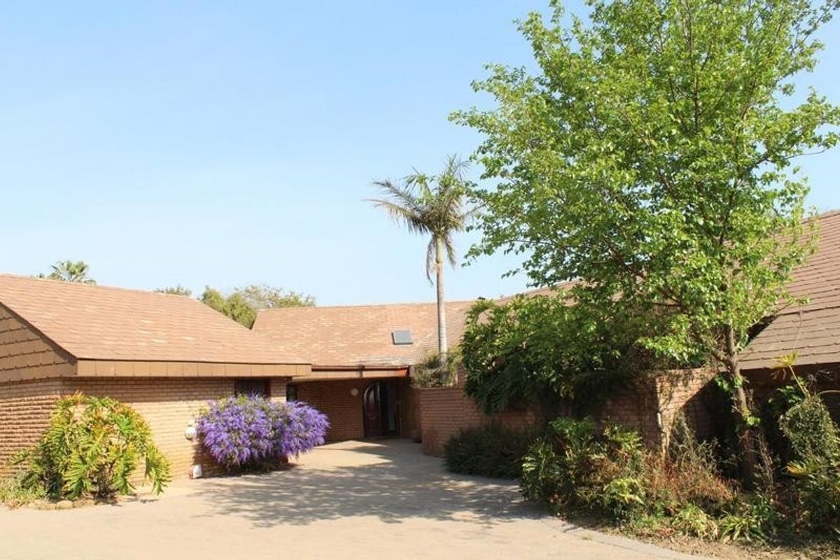 Front elevation of a brick-built small holding featuring a tiled roof, paved driveway, and established garden surroundings.