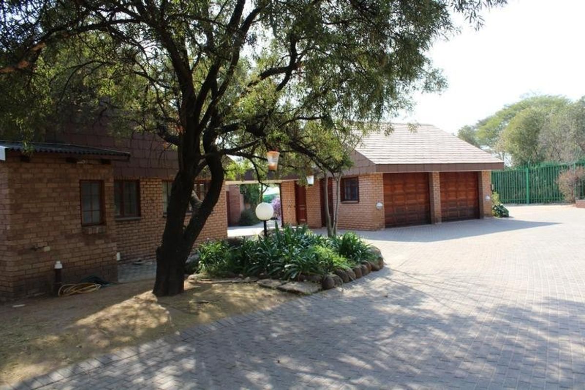 Front view of the property featuring a facebrick exterior, a paved driveway, and a double garage with wooden doors.