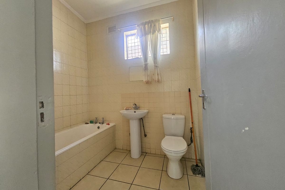A dated bathroom featuring a standard bathtub, pedestal basin, and toilet with original ceramic tiling throughout.