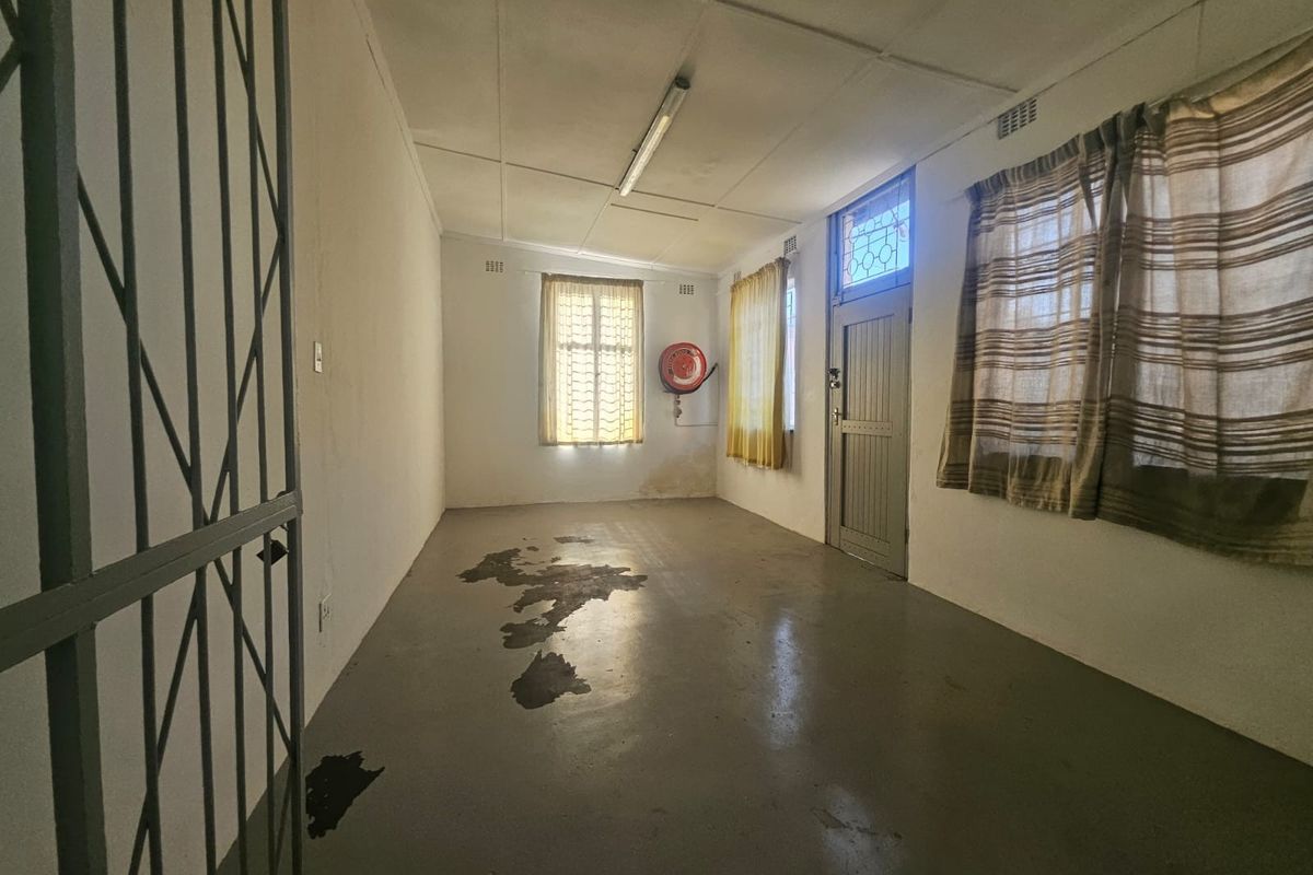 An empty commercial office space featuring painted concrete floors, a security gate, and a wall-mounted fire extinguisher, requiring cosmetic refurbishment.