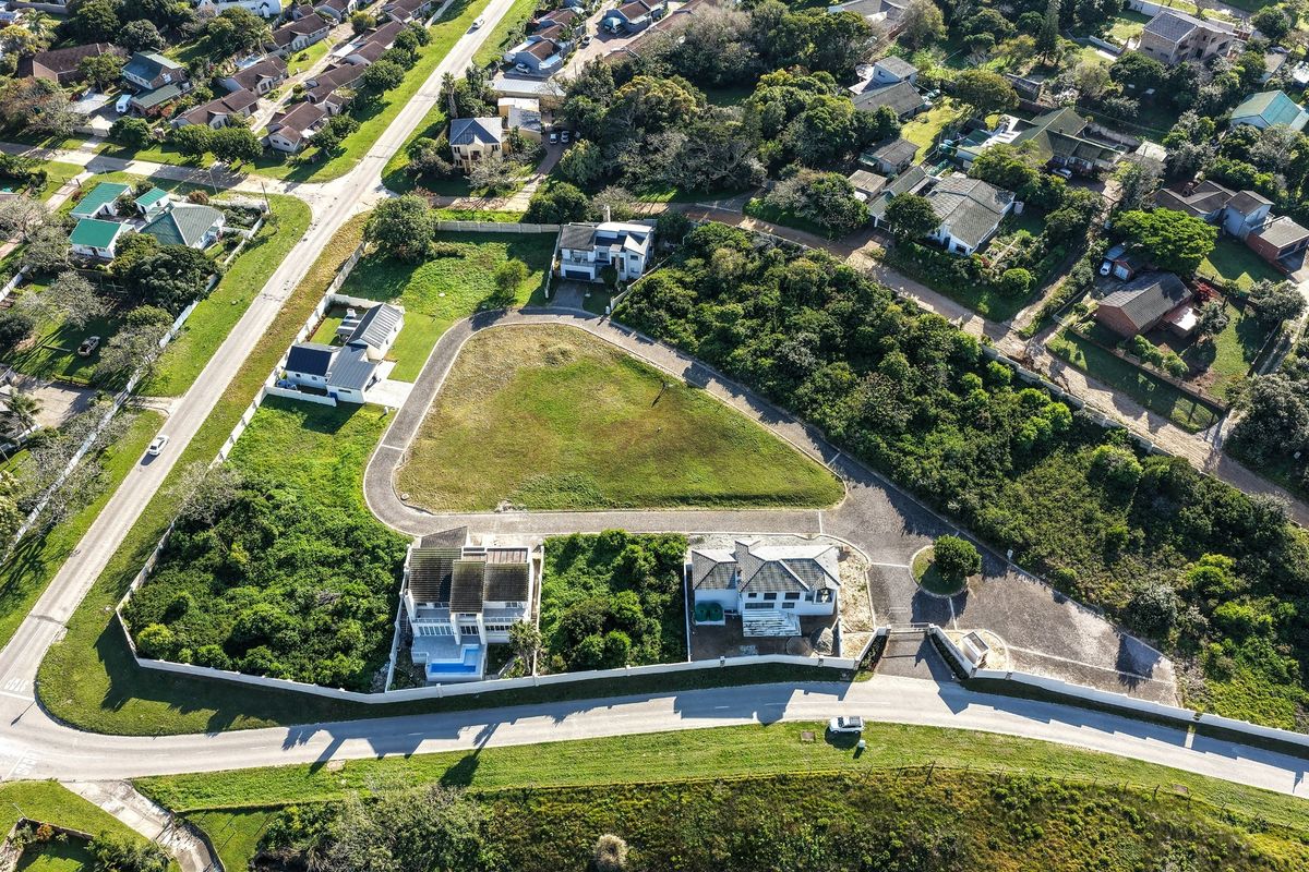 Aerial view of a vacant residential plot featuring a paved driveway, boundary walls, and gated access within an established neighborhood.