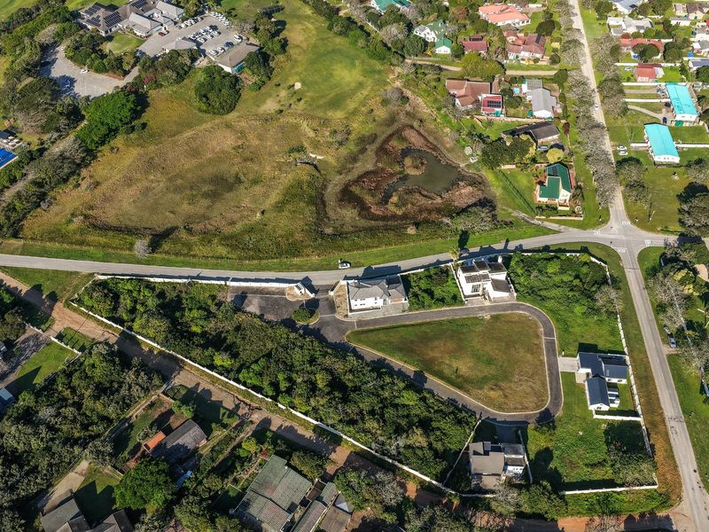 Aerial view of a residential vacant land plot featuring a paved driveway, established boundary walls, and surrounding greenery in a suburban neighborhood.